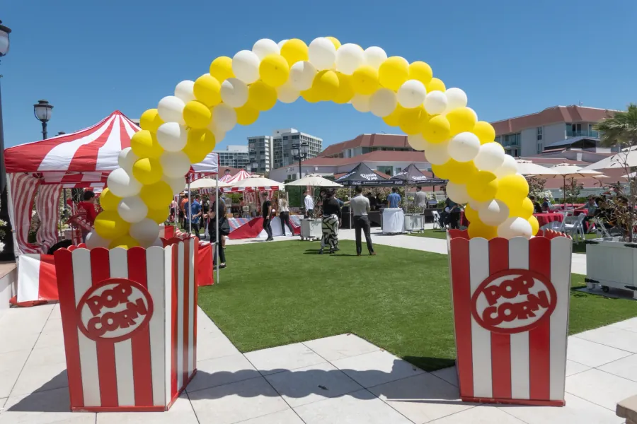 Popcorn stand under a balloon arch at a corporate family day carnival