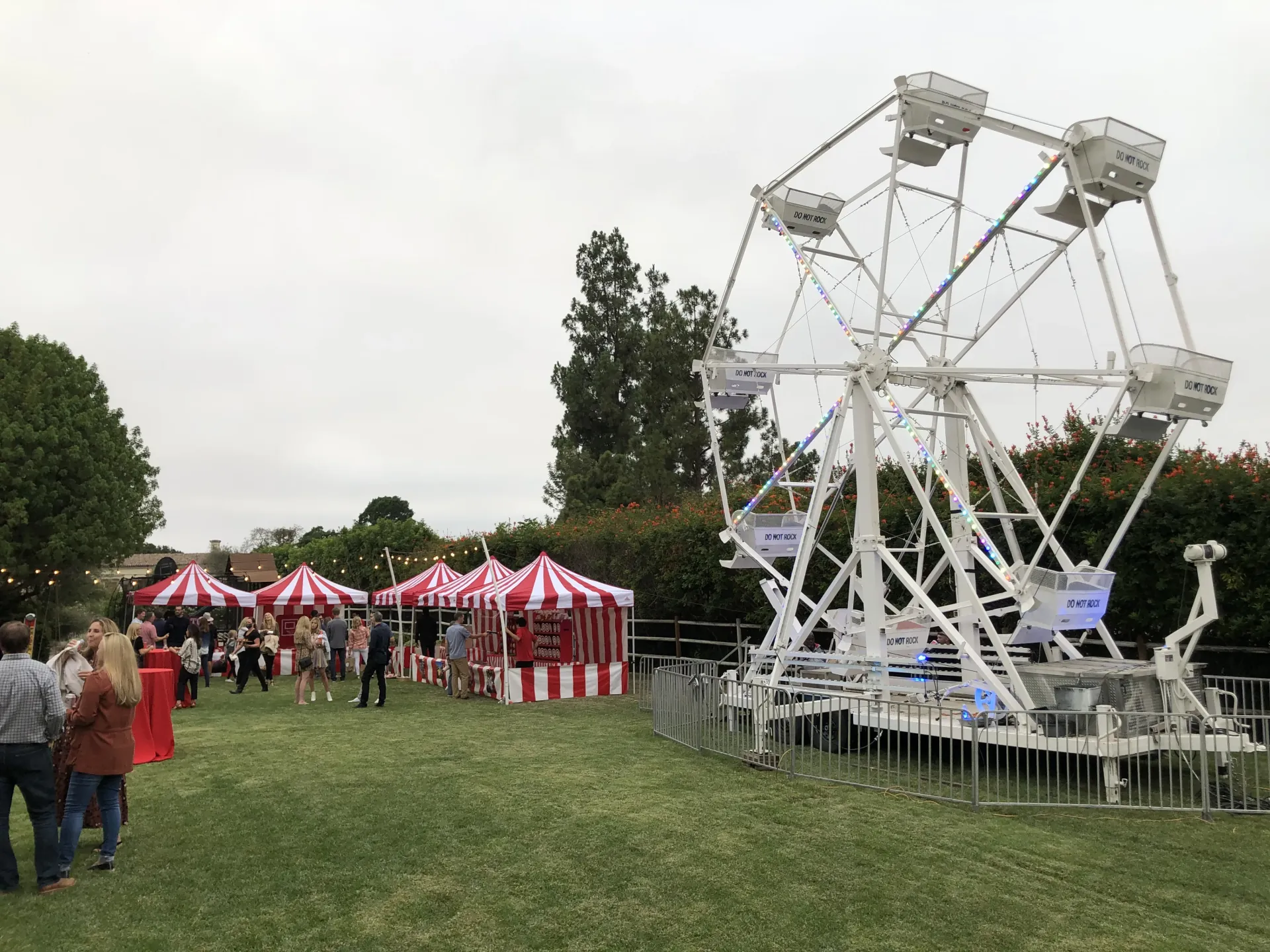 A mini ferris wheel and trackless train set up on an open grass field at a rural community festival