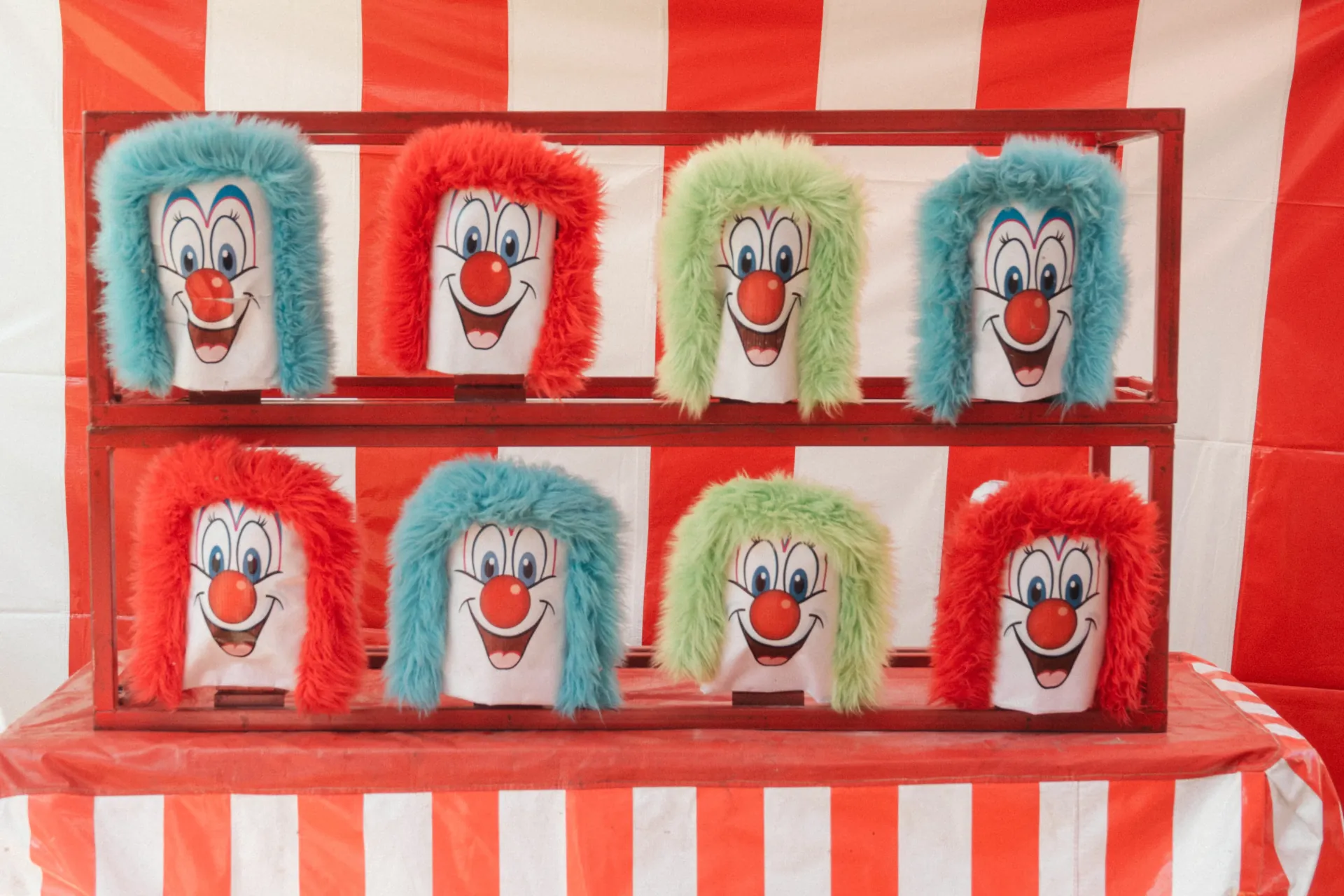 A carnival game midway of six to eight booths set up at a park pavilion, families walking between game stations