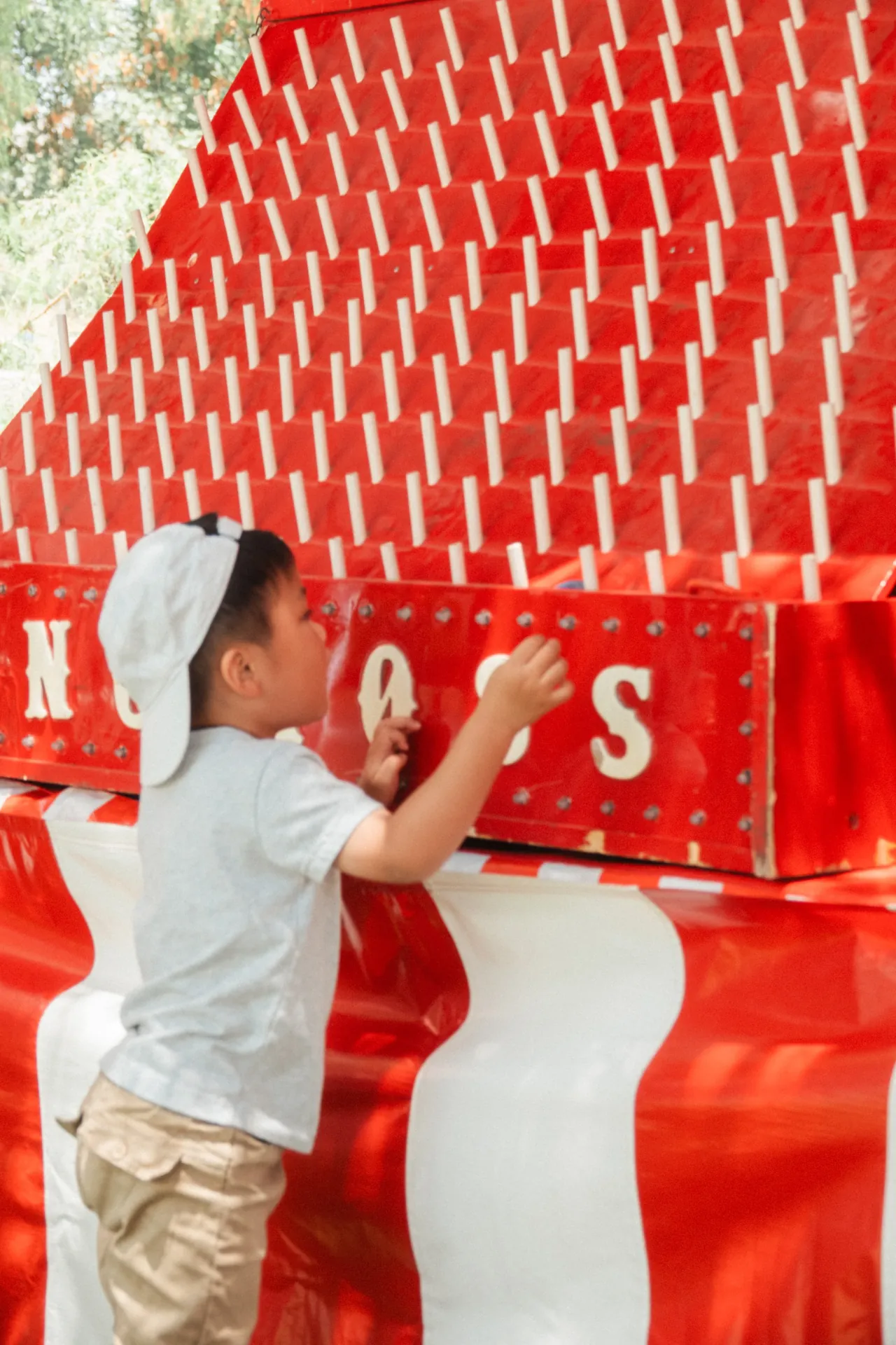 Children playing a carnival game at an outdoor community event, with an attendant handing out prizes near a row of striped booths