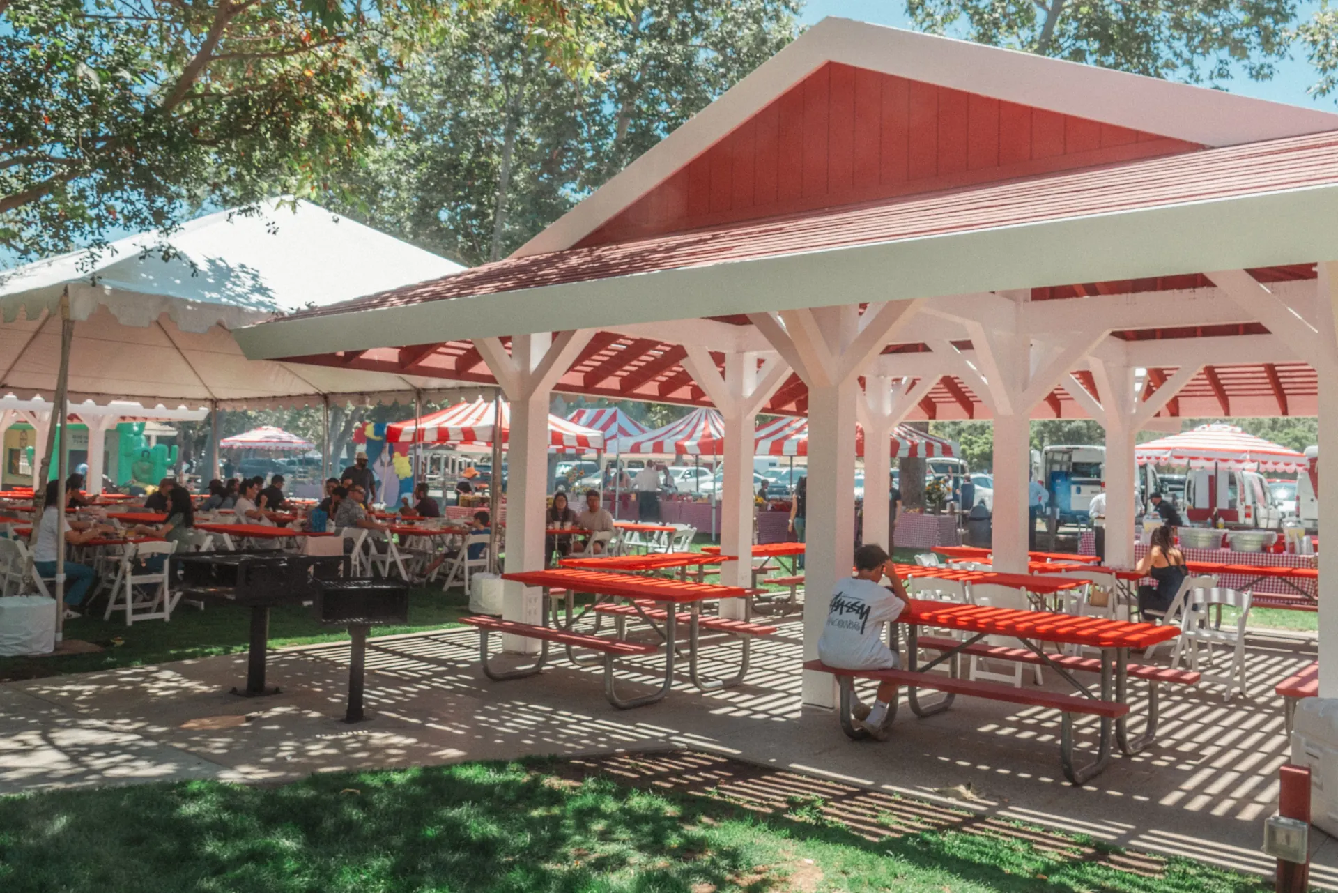 A company family day set up on open turf with striped carnival game booths, an inflatable bounce house, and families gathered under a picnic shelter in Alpine, CA