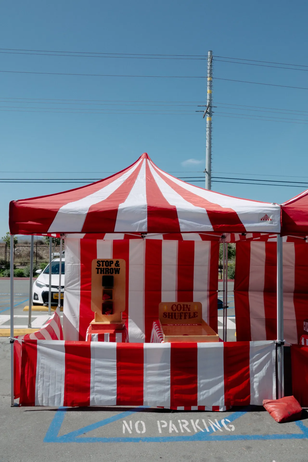 An attendant in a striped vest running a ring-toss booth at an outdoor company picnic with families in the background