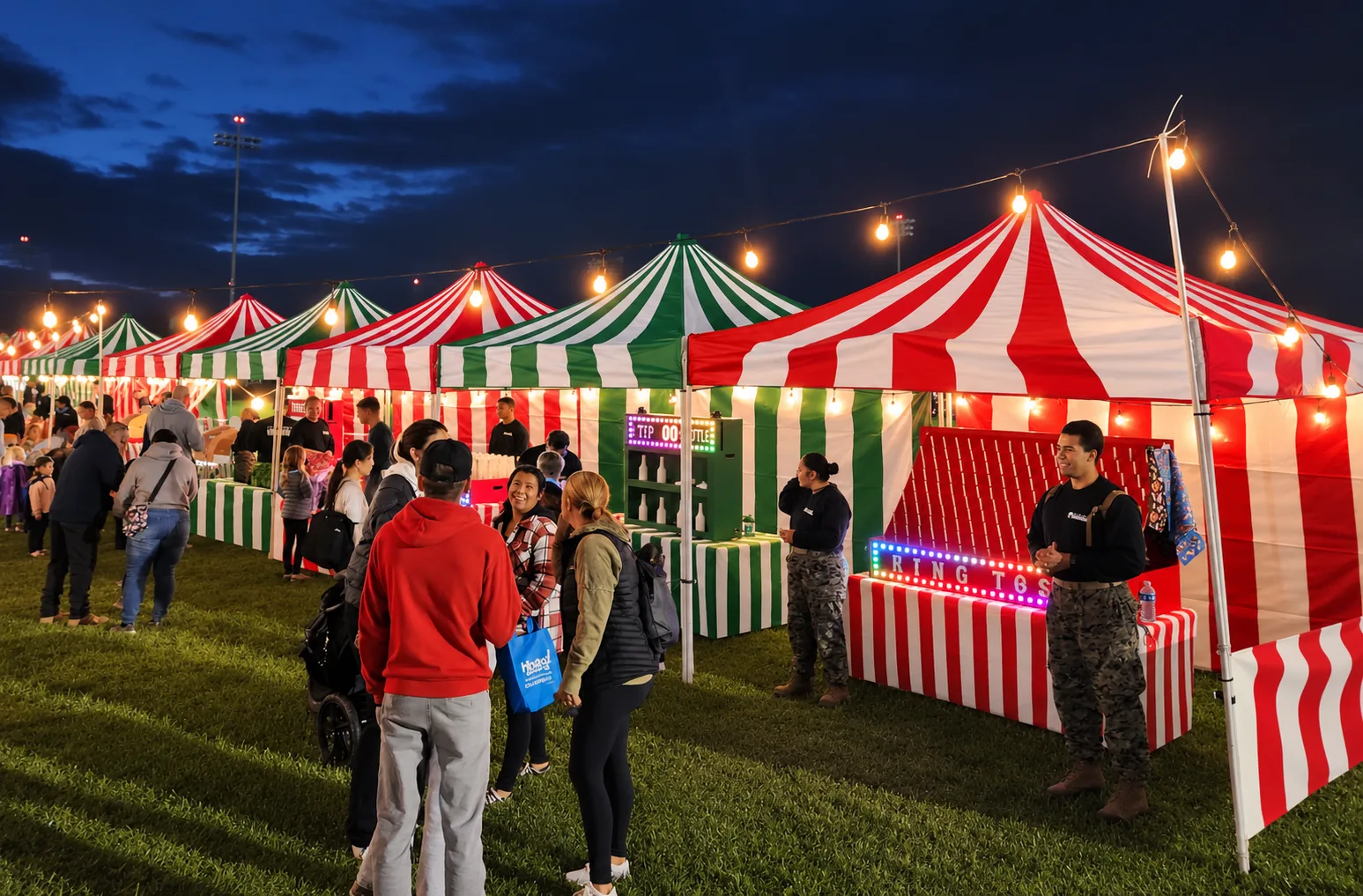 Red-and-white and green-and-white striped carnival booths under string lights at dusk, with a lit ring-toss marquee, at an outdoor winter holiday event in Eastlake, CA